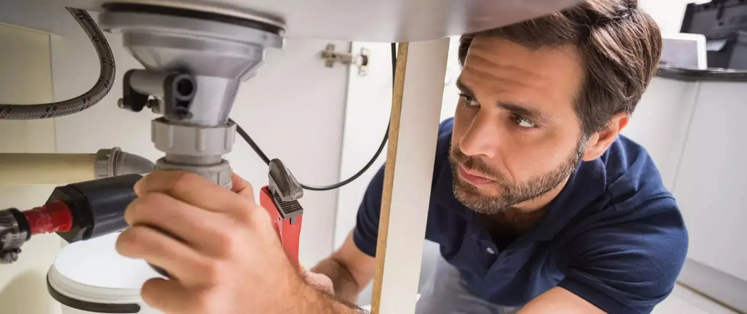 Gasfitero ajustando con una llave la tubería de agua bajo el lavadero de una cocina