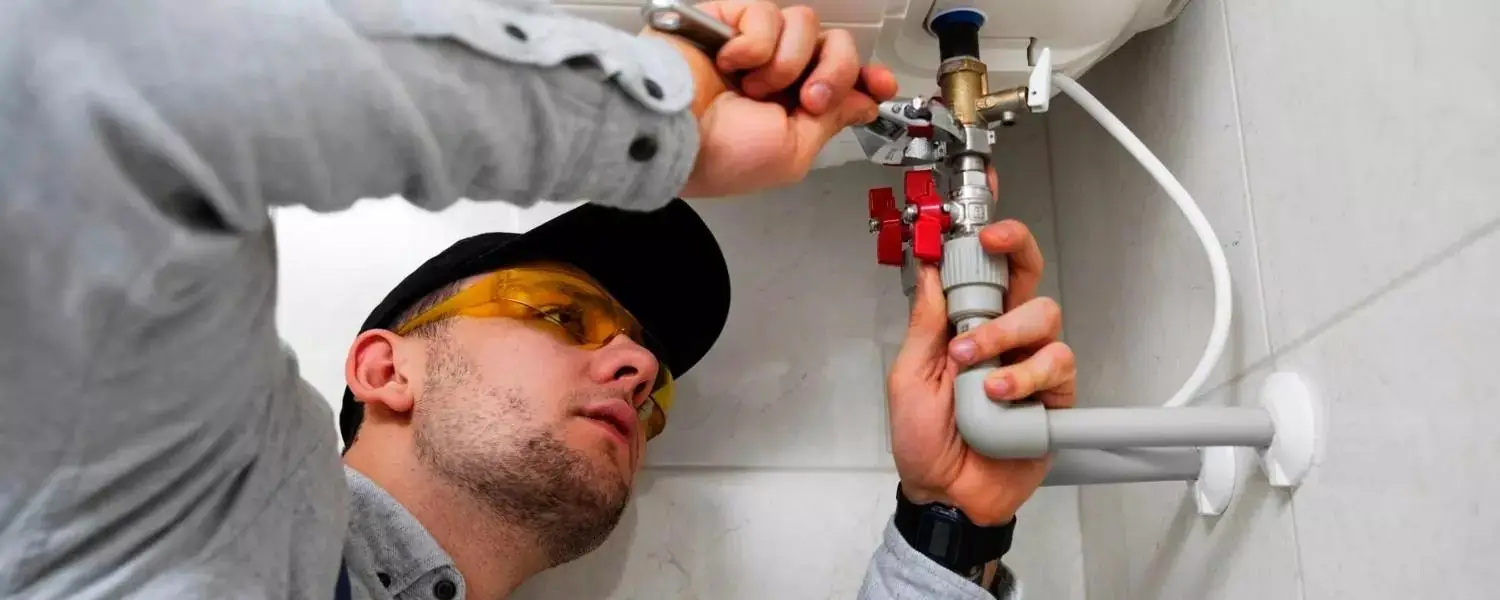 Gasfitero con lentes de seguridad ajustando una llave de manija roja en la conexión de agua de una terma